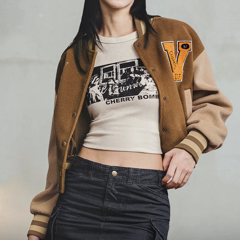 Person wearing a brown letterman jacket over a graphic t-shirt with text on a gray background
